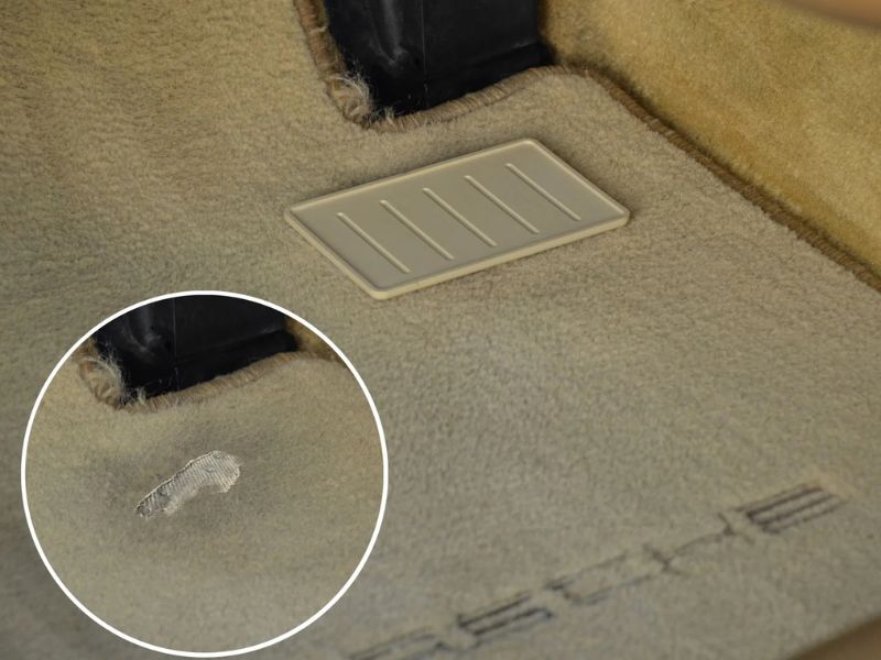 A worn-out car floor mat with a hole near the driver's heel position, exposing the factory carpet.