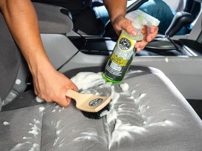 Cleaning car seat upholstery with a microfiber towel and interior cleaner.