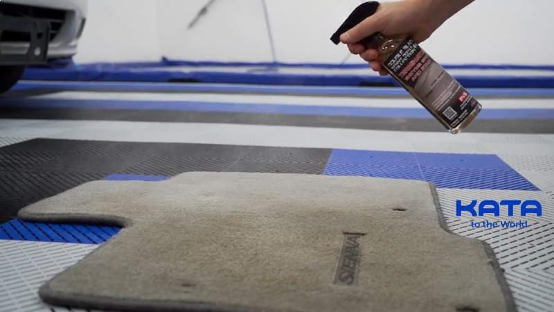 Applying a car-safe enzyme cleaner to a removable car floor mat to break down organic waste and eliminate dog poop odors.